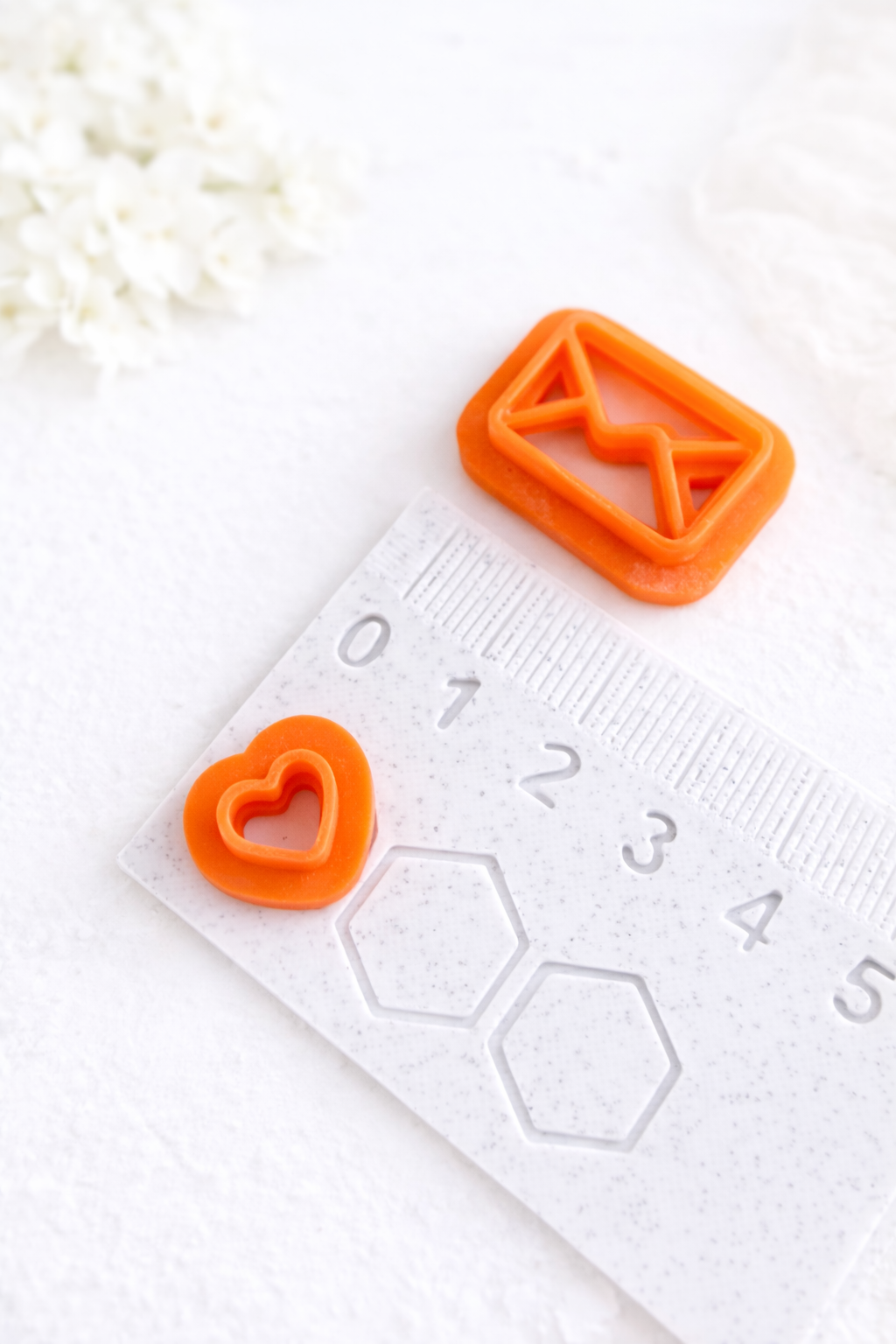 A 3D printed polymer clay cutter set beside a ruler and a heart polymer clay cutter on the opposite side of the ruler, on a white background. 