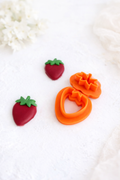 Strawberry polymer clay cutter set, strawberry clay cutter bottom and strawberry green clay cutter top lay on a white background with the polymer clay strawberry product beside it as an example. 
